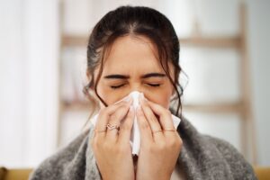 Woman blowing nose with shelf in background