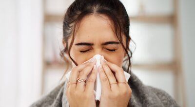 Woman blowing nose with shelf in background